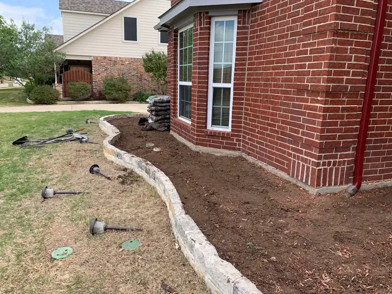Stone-edged bed along a brick wall with irrigation heads exposed mid-job in Fort Worth