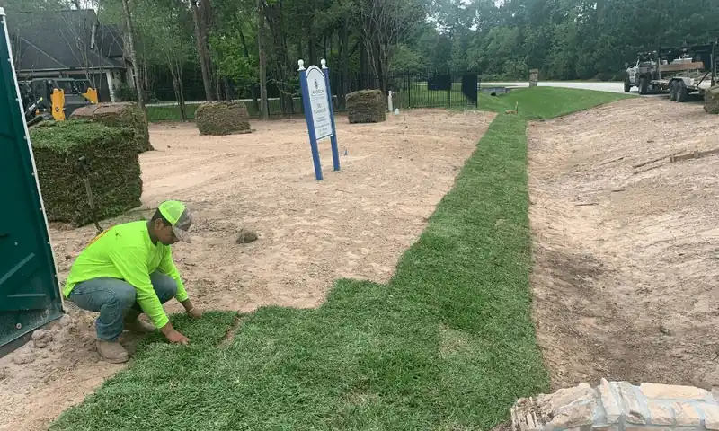 Hoyer's crew member in a hi-vis shirt laying new sod rolls on a prepared sand bed