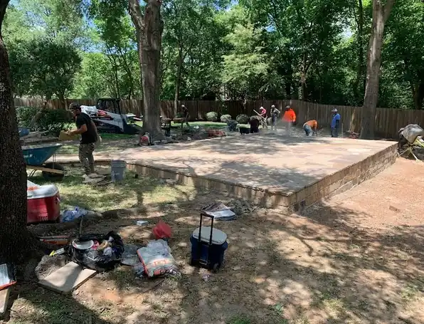 Crew building a paver patio under mature trees